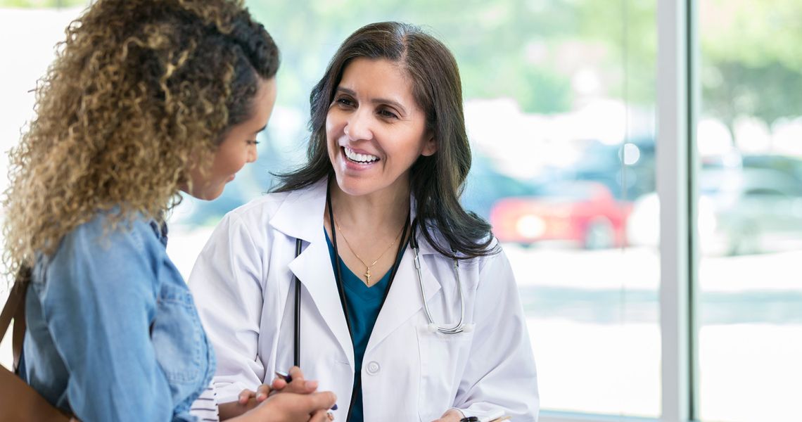 A doctor in a white coat with a stethoscope talks to a patient